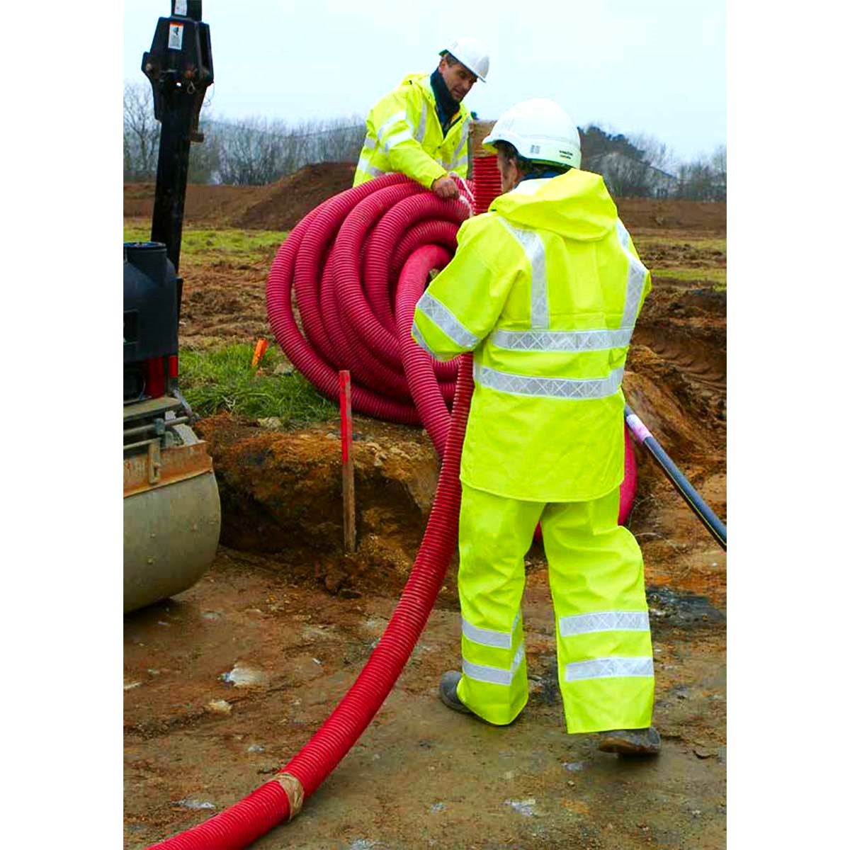 Two workers in Guy Cotten Isoflash Poulflash high-visibility clothing handling a large red hose on a construction site.