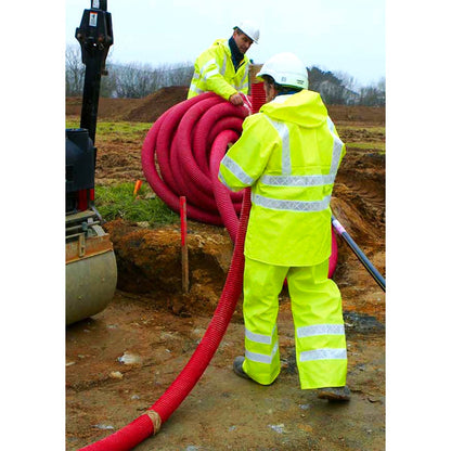 Two workers in Guy Cotten Isoflash Poulflash high-visibility clothing handling a large red hose on a construction site.